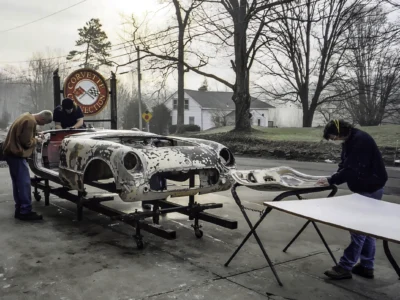 1954 Corvette body on rotisserie outdoors showing front end and headlight buckets at Corvette Connection