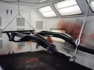 1954 Corvette body structure hanging in paint booth showing bare fiberglass at Corvette Connection