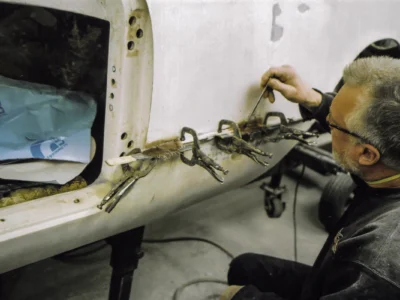 Technician fitting door hinges on 1954 Corvette fiberglass body during restoration at Corvette Connection