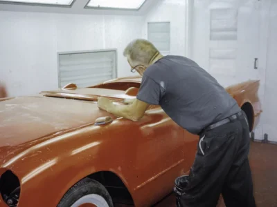 Technician wet sanding 1954 Corvette hood in red paint in paint booth at Corvette Connection