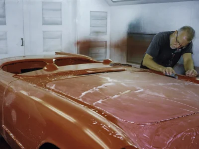Technician wet sanding 1954 Corvette body in red paint in paint booth