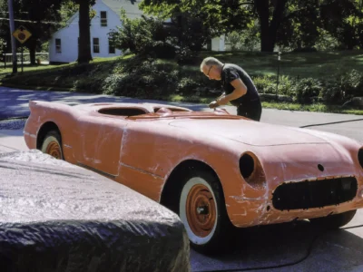 Technician inspecting 1954 Corvette body in red primer during restoration at Corvette Connection