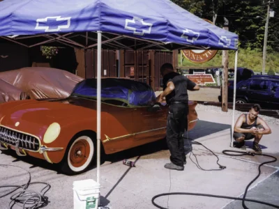 Owner detailing completed 1954 Corvette in red under tent at car show