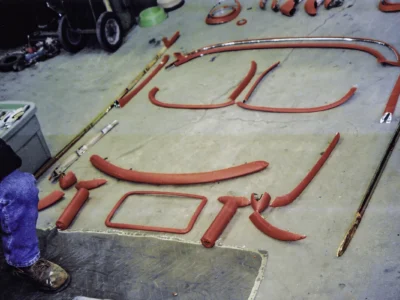 1954 Corvette freshly painted red frame components and brackets organized on shop floor