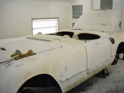 1954 Corvette body in white primer in paint booth showing headlight openings at Corvette Connection
