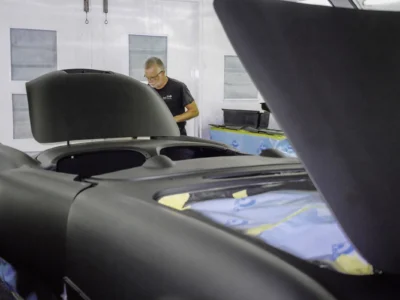 Technician spraying black sealer coat on 1954 Corvette body in paint booth