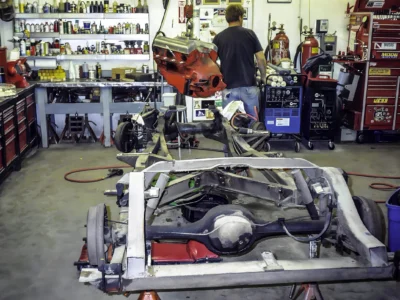 Technician working on 1957 Corvette chassis and exhaust in shop at Corvette Connection