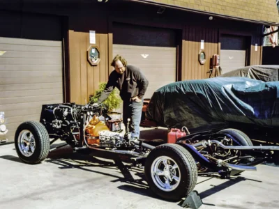 Technician working on 1957 Corvette engine on rolling chassis with body covered at Corvette Connection