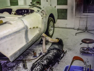Technician working underneath 1957 Corvette body during fiberglass repair at Corvette Connection