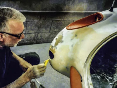 Technician hand-sanding body filler on 1957 Corvette during fiberglass repair