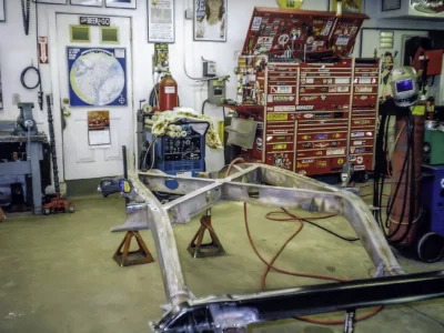 1957 Corvette bare frame on jack stands with technician welding at Corvette Connection