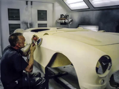 Technician sanding 1957 Corvette body in primer inside paint booth at Corvette Connection