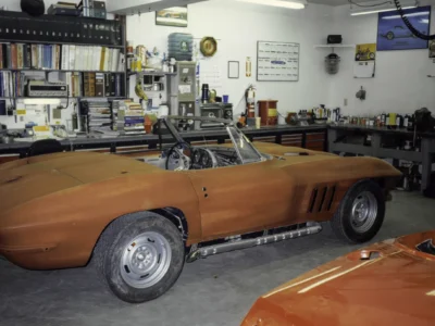 1965 Corvette Sting Ray engine on stand with orange Corvette in background at Corvette Connection