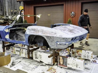 1966 Corvette Sting Ray body on rotisserie outdoors with technician doing fiberglass work