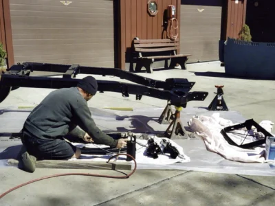 Technician working on a restored 1968 Corvette frame outside the shop