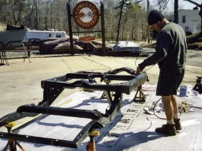Technician moving or positioning a restored 1968 Corvette frame outside Corvette Connection.