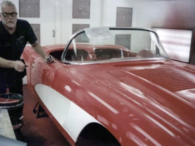Side profile of red and white 1958 Corvette during reassembly with door open