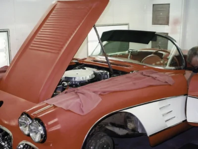Front three-quarter of red 1958 Corvette with hood up showing engine bay during reassembly