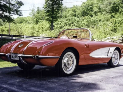Finished red and white 1958 Corvette parked outdoors with trees behind