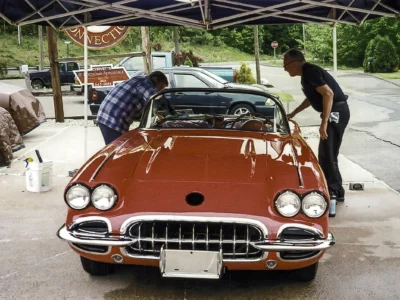 Owner standing beside finished red and white 1958 Corvette under canopy at outdoor show