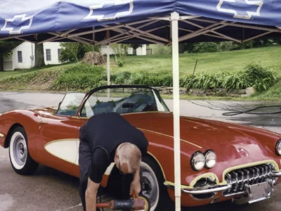 Owner kneeling beside finished red and white 1958 Corvette polishing at outdoor show