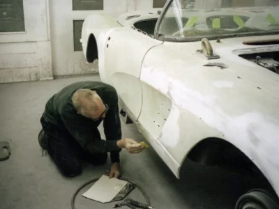 Corvette Connection technician kneeling beside 1958 Corvette body during sanding stage