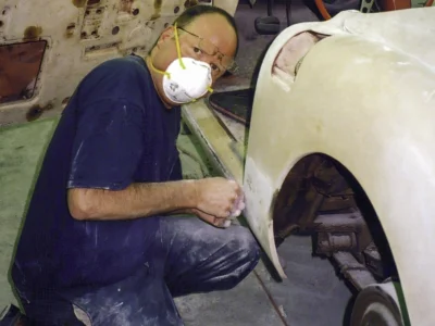 Technician with dust mask sanding 1958 Corvette front fender wheel opening at Corvette Connection
