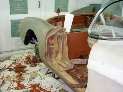 1958 Corvette body shell with red overspray on shop floor during paint preparation