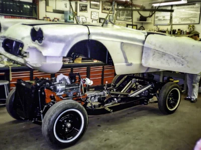Side profile of 1962 Corvette body in primer mounted on rolling chassis during assembly