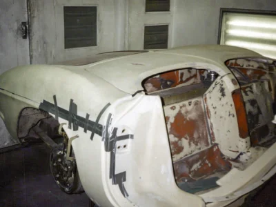 Remastered photo of a 1957 Chevrolet Corvette body restoration in progress at Corvette Connection in Bolton, Connecticut, showing stripped rear bodywork, primer, and exposed interior structure