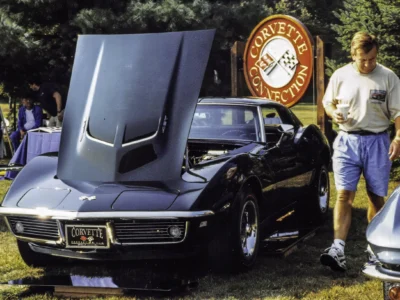 Owner standing next to completed 1968 Corvette Stingray in black at Corvette Connection sign