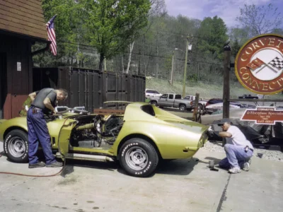 Technician working near the rear of a gold 1969 Corvette convertible outside the shop.