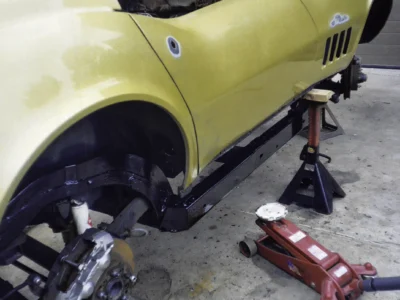 Close-up of gold 1969 Corvette lower body and rear wheel area on jack stands.