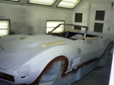 1969 Corvette side body in light primer with red bodywork areas visible.