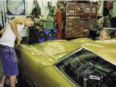 Technician polishing the roof and rear deck of a gold 1969 Corvette.