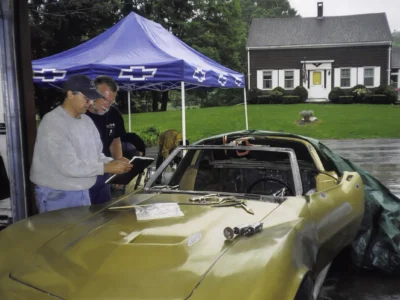 Technician working on a gold 1969 Corvette under a canopy outside the shop.
