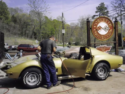 Technician working beside a gold 1969 Corvette convertible with the door open.