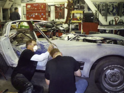 Technicians sanding and aligning a 1970 Corvette body during restoration.