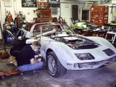 Technicians working on the front body section of a 1970 Corvette inside the shop.