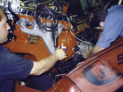 Technician installing engine components on a red 1970 Corvette during mechanical assembly.