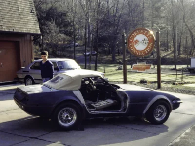 McBurnie Daytona Spyder in dark primer outdoors at Corvette Connection with shop sign visible