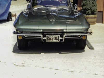 Remastered photo of a green 1965 Chevrolet Corvette convertible front view photographed outside Corvette Connection in Bolton, Connecticut, showing the chrome bumper, hood detail, and restored front end.