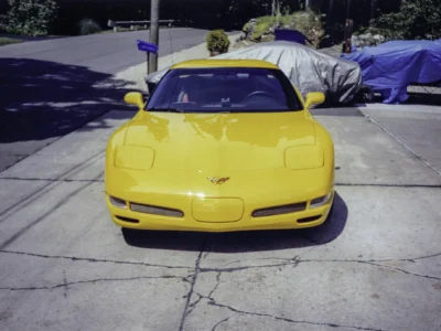 Remastered photo of a yellow 1999 Chevrolet Corvette coupe front view outside Corvette Connection in Bolton, Connecticut, showing the C5 body style and restored exterior finish.