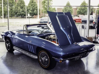 Remastered photo of a blue 1966 Chevrolet Corvette convertible rear side angle with hood open outside Corvette Connection in Bolton, Connecticut, showing restored paint, chrome trim, and engine bay display.