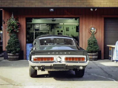 Remastered photo of a white classic Ford Mustang rear view inside the Corvette Connection shop in Bolton, Connecticut, showing the rear taillight panel, bumper, and restored exterior finish.