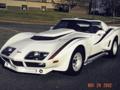 Remastered photo of a white custom Chevrolet Corvette coupe front angle, showing a raised hood scoop, wide body styling, and performance-focused restoration details by Corvette Connection.