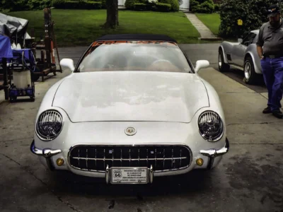 Remastered photo of a white 1957 Chevrolet Corvette convertible front view, showing the chrome grille, round headlights, red interior, and restored classic Corvette bodywork.