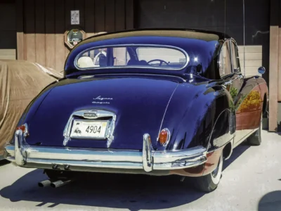 Remastered photo of a black Jaguar Mark II rear view, showing the classic rounded rear body, chrome bumper, trunk badge, and restored dark paint finish.