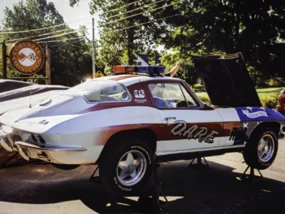 Remastered photo of a patriotic red, white, and blue 1970s Chevrolet Corvette pace car rear side angle, showing custom paint, graphics, and classic Corvette bodywork.