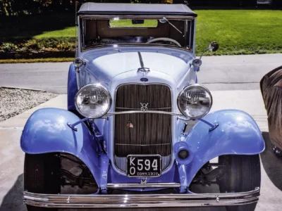 Remastered photo of a blue 1930s classic convertible front view, showing the chrome grille, round headlights, hood ornament, and restored vintage bodywork.